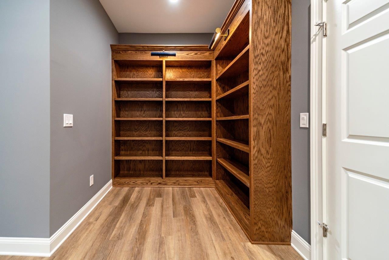 Built-in wooden bookshelves in a gray-walled room with light wood flooring. A white door is on the right.