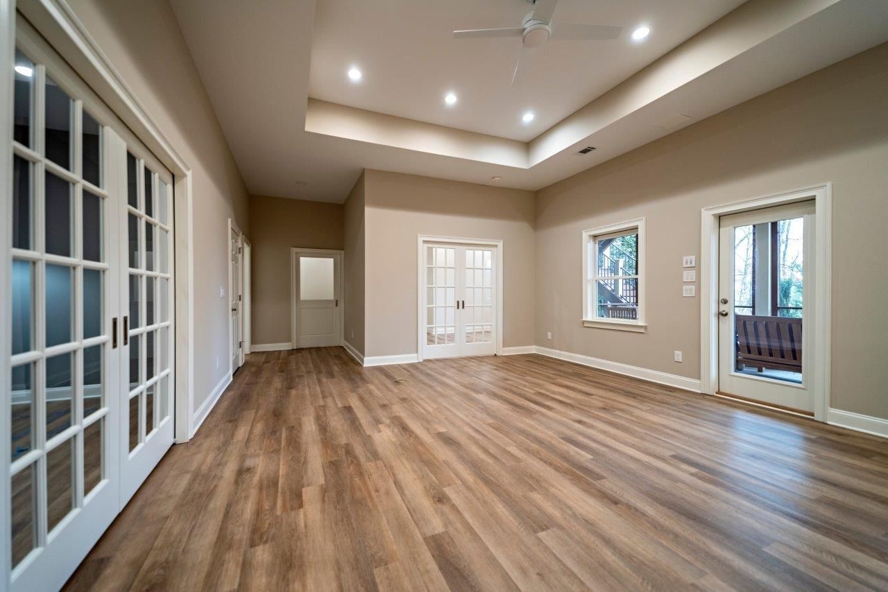 Empty room with hardwood floors, recessed lighting, and several doors leading to other areas.