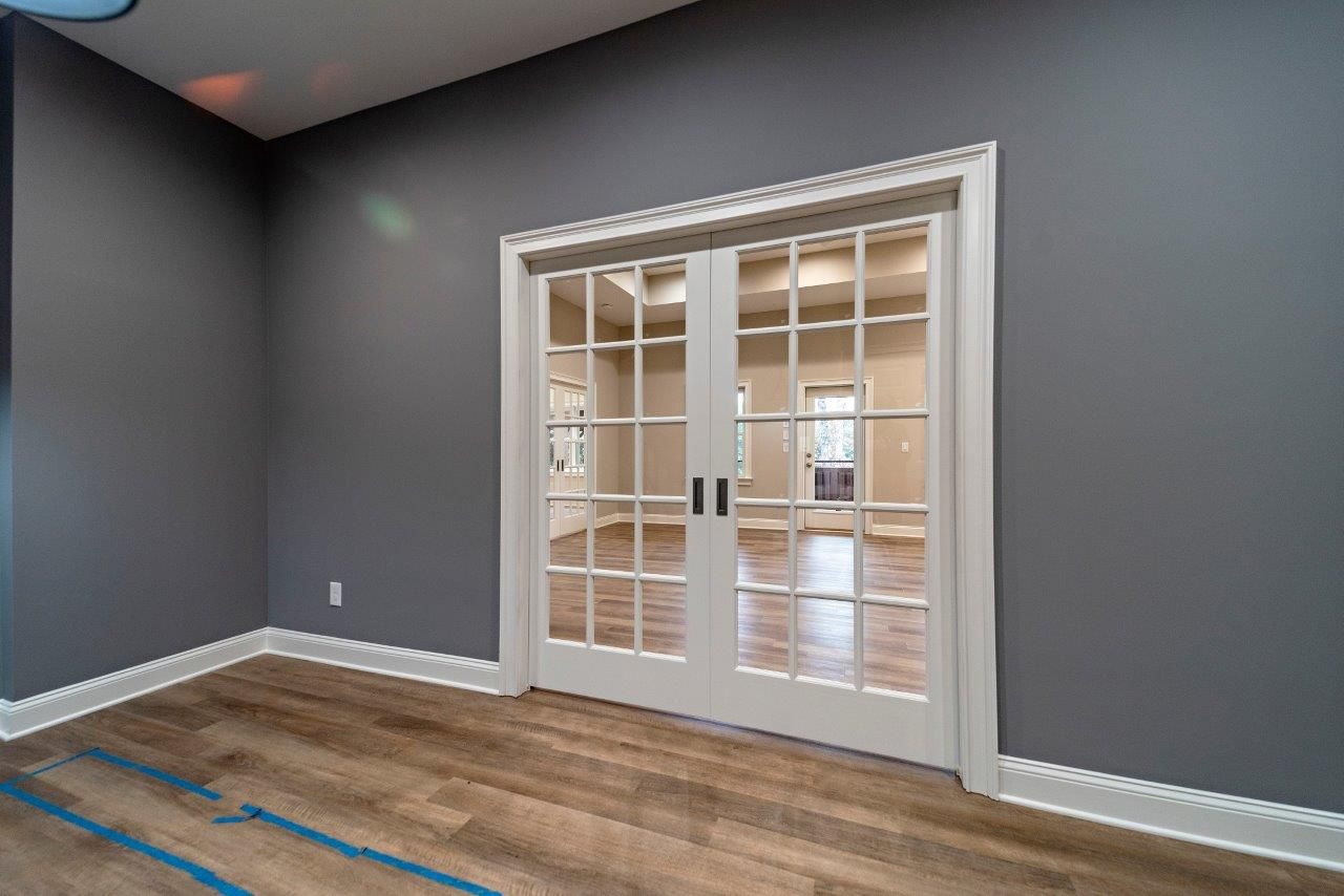 Gray-painted room with French doors. Light wood floor, white trim. Door leads to another room.