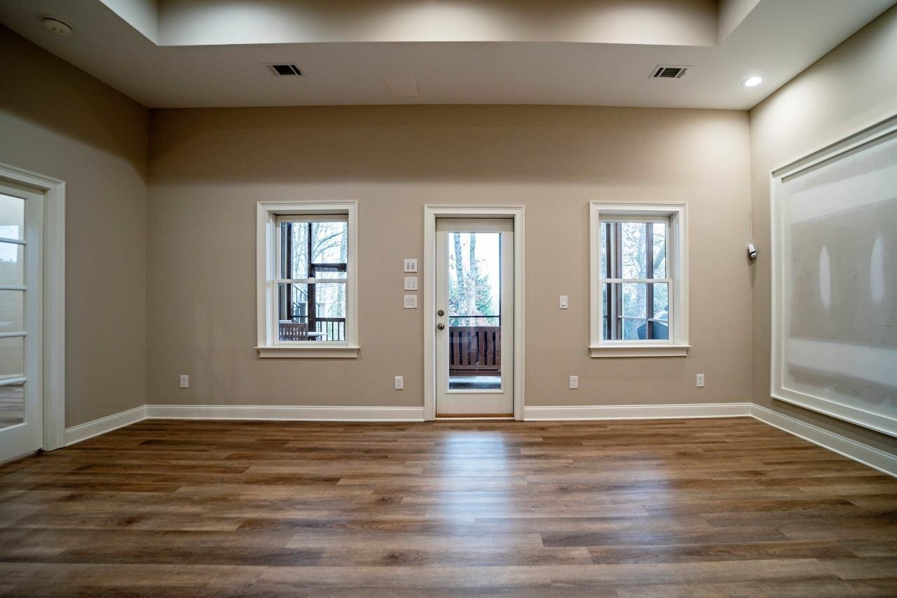 Empty room with wooden floor, tan walls, and three windows looking outside.