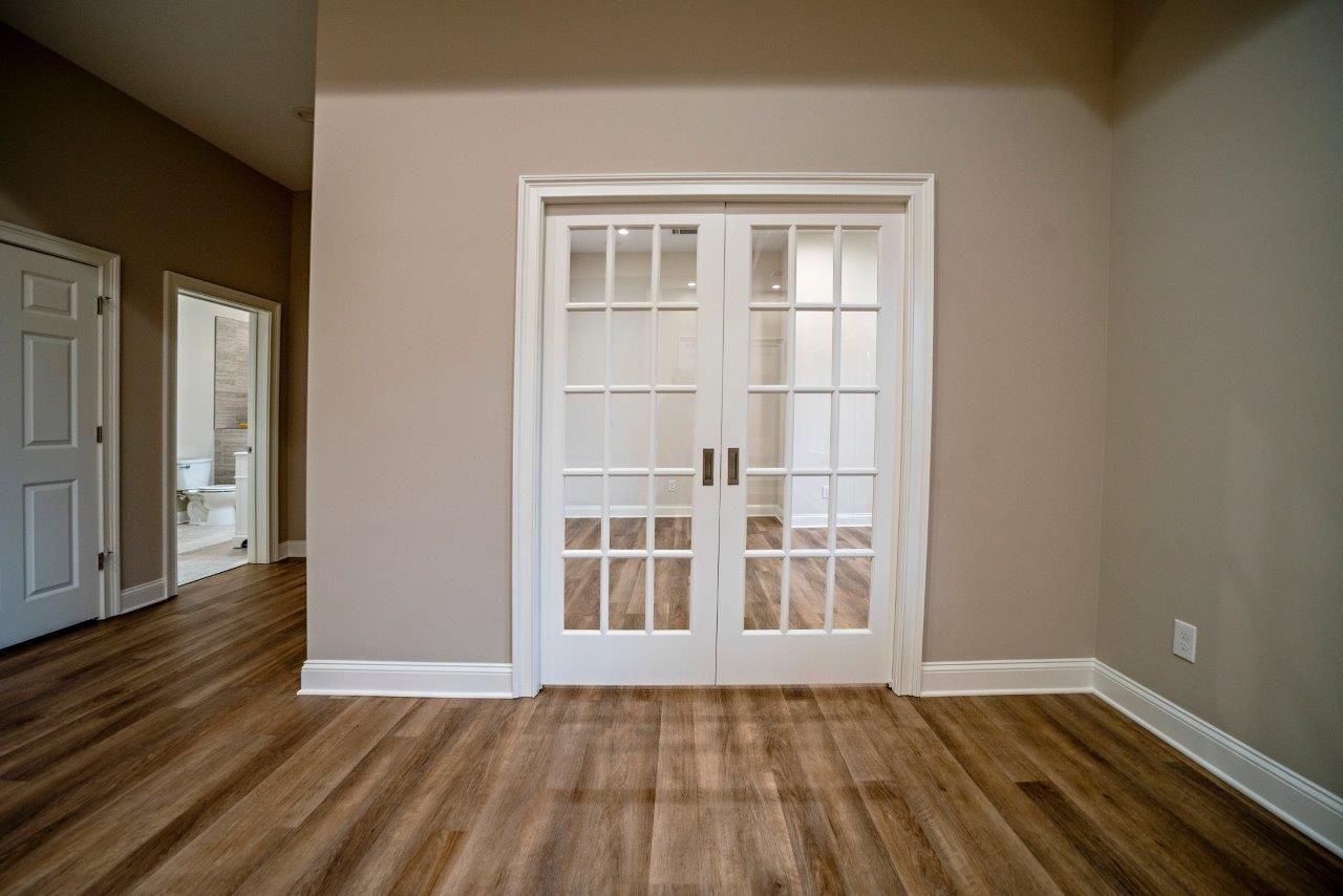 Interior view of a room with french doors, beige walls, and wood-look flooring. A door is on the left.
