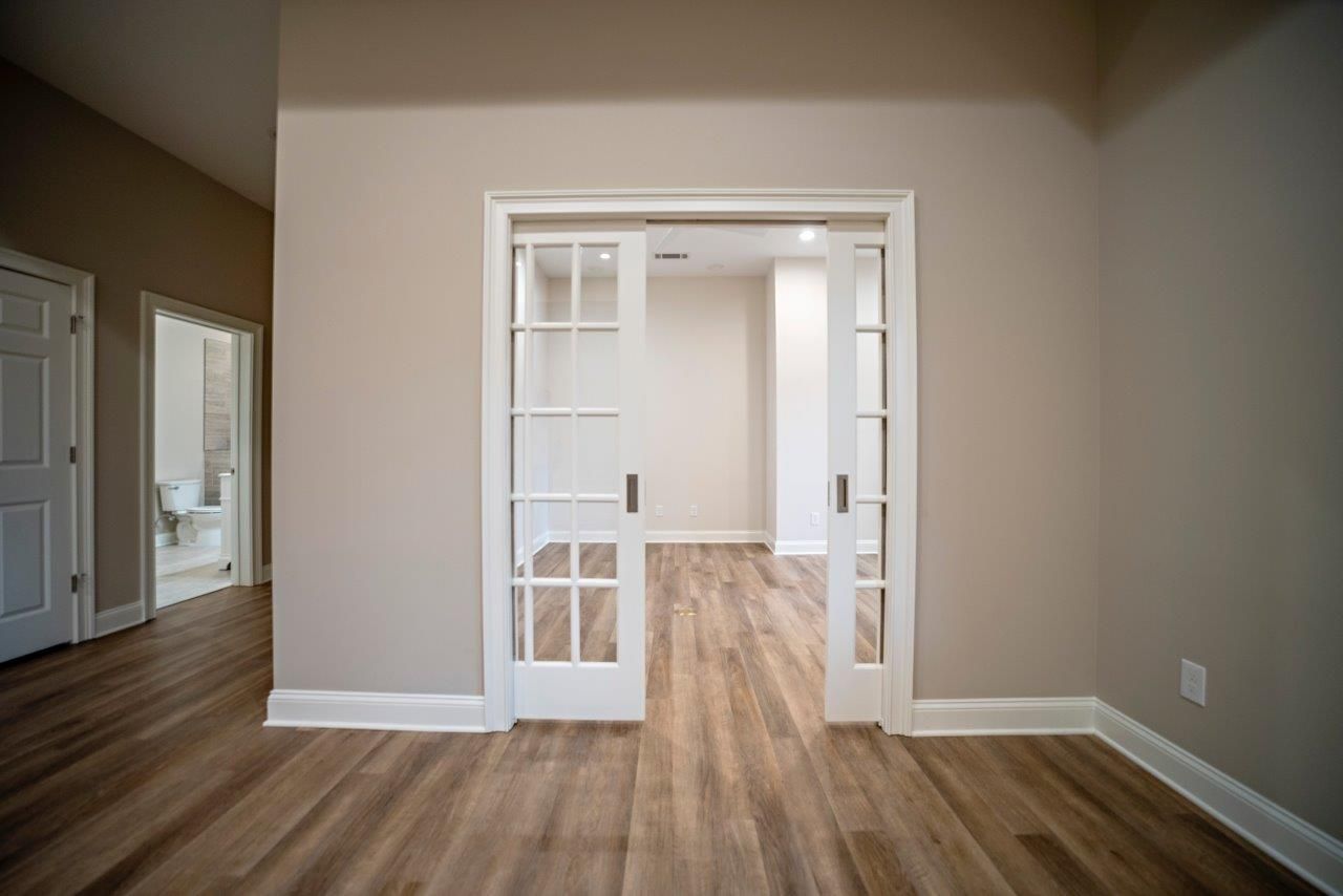 Interior view: sliding glass doors leading to a room with hardwood floors. Beige walls, white trim and doors.