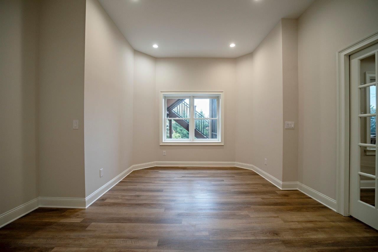 Empty room with hardwood floors, a window, and a white door.