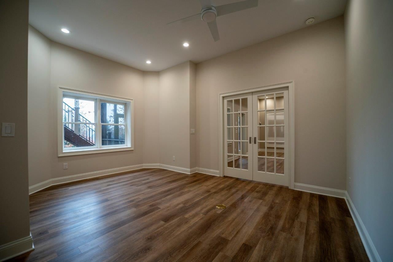 Empty room with wood-look floor, French doors, window, and recessed lighting. Beige walls and white trim.