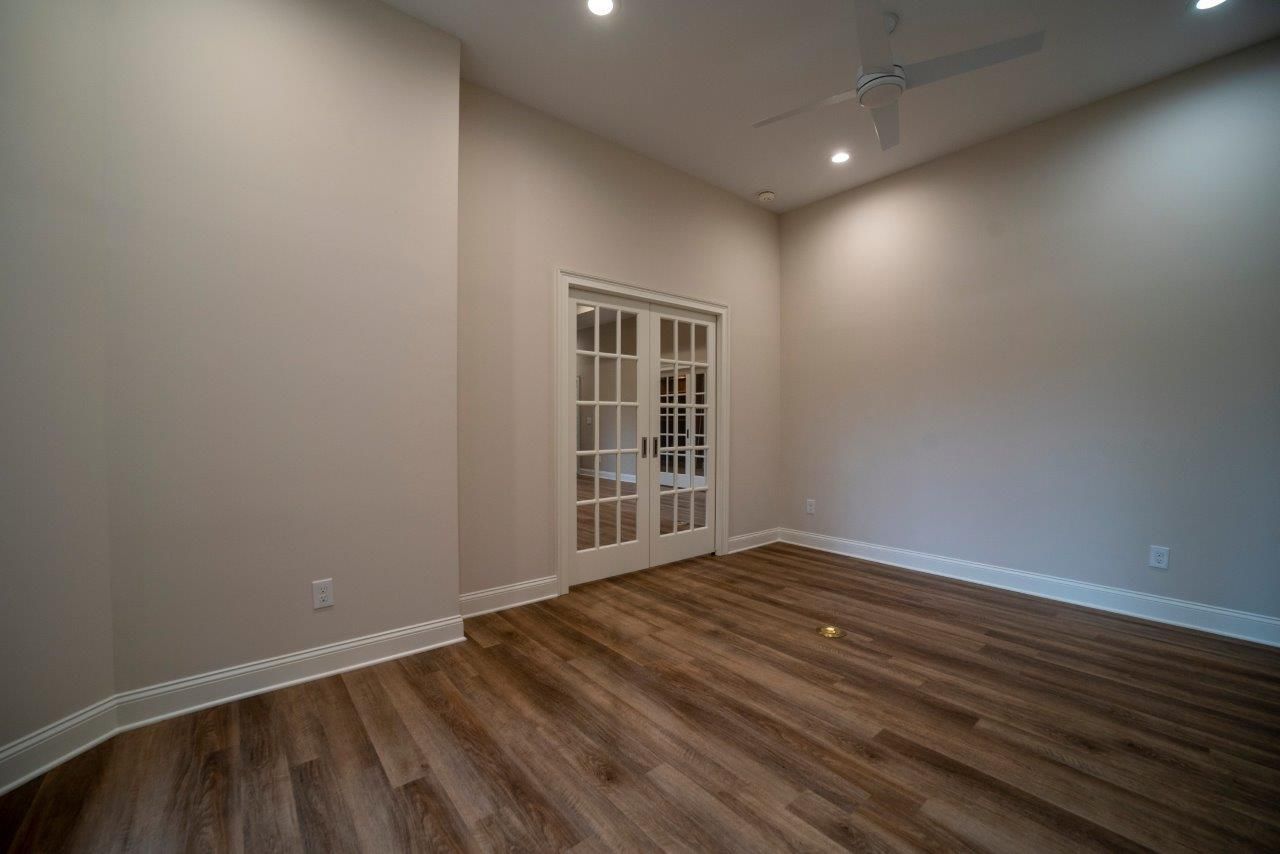 Empty room with French doors, wooden floors, and beige walls.