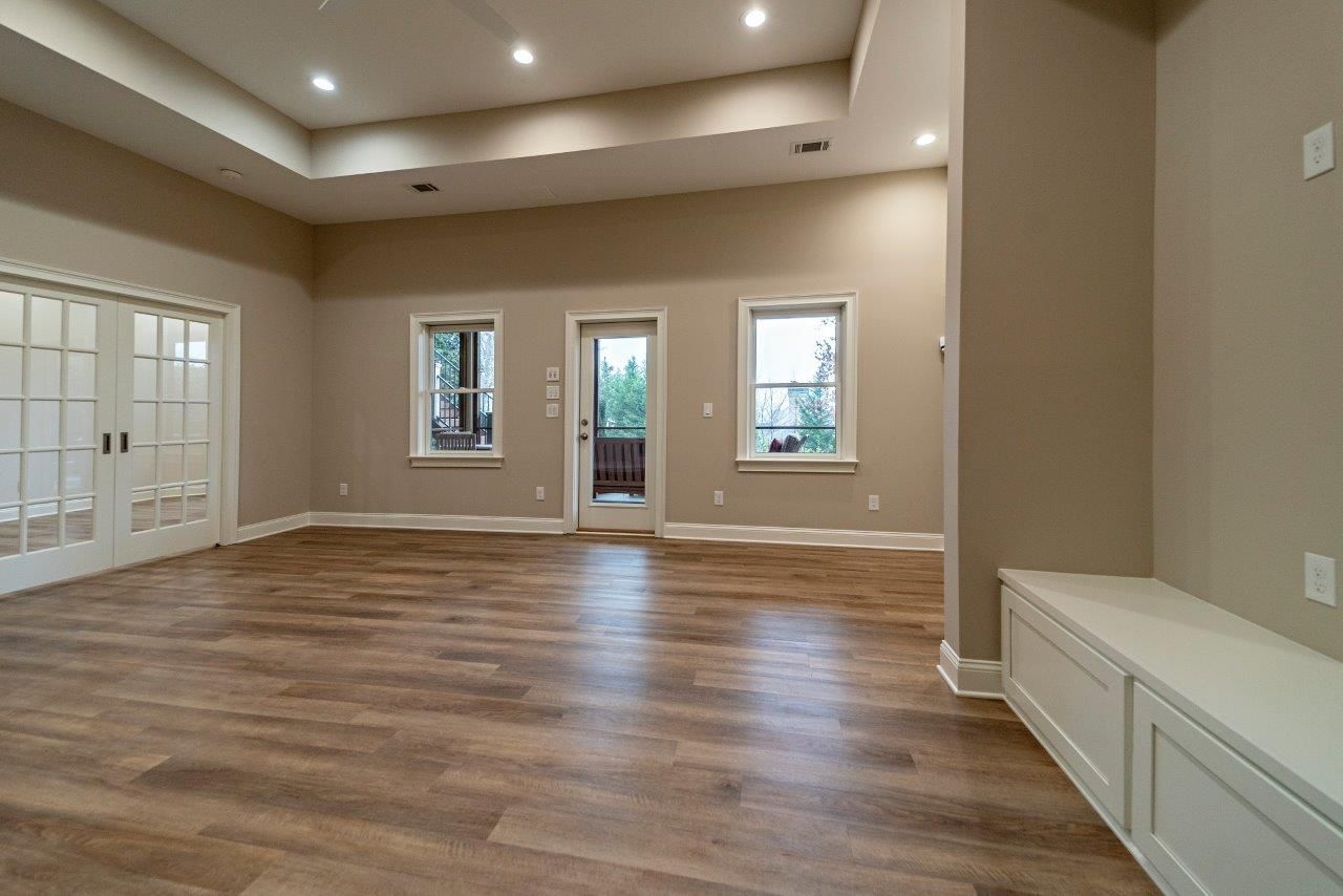 Empty, bright interior room with wood flooring, beige walls, and white accents, featuring French doors and outdoor access.