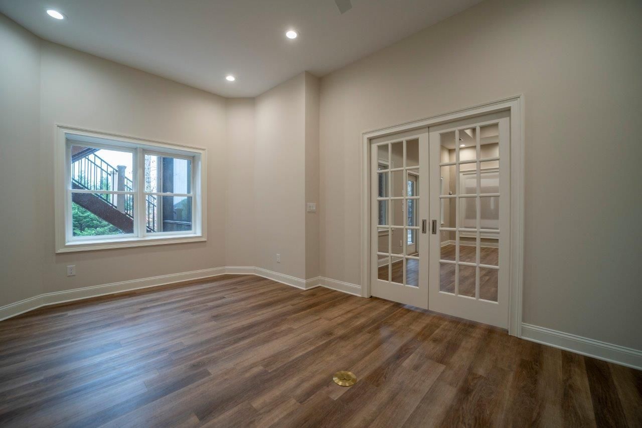 Empty room with wooden floors, French doors, and a window.