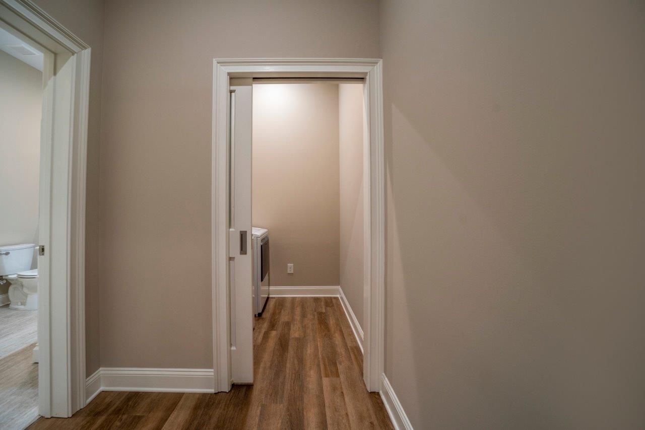Hallway with doorways, neutral-colored walls, and hardwood floors. Laundry room visible in the center doorway.