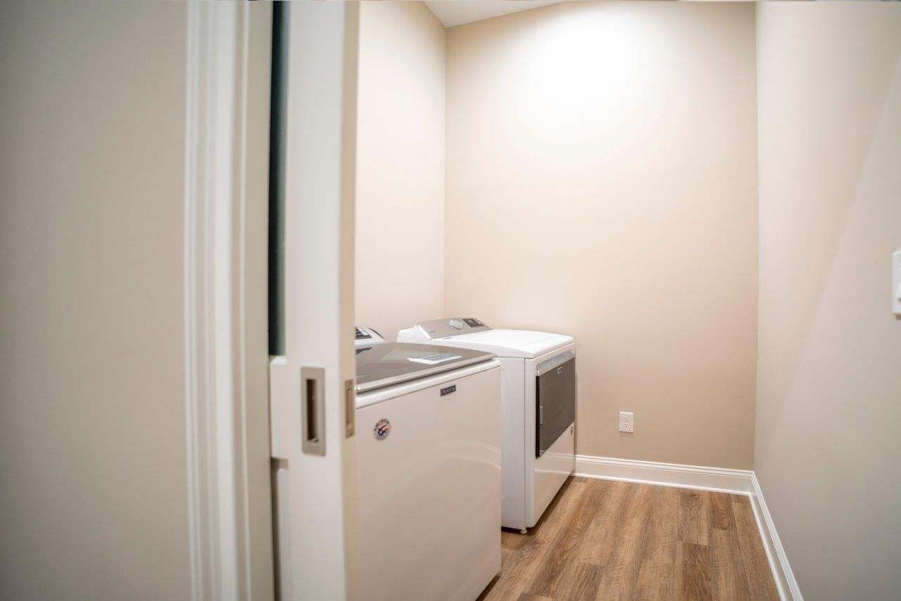 Laundry room with washing machine and dryer, neutral walls, wood-look floor, pocket door.