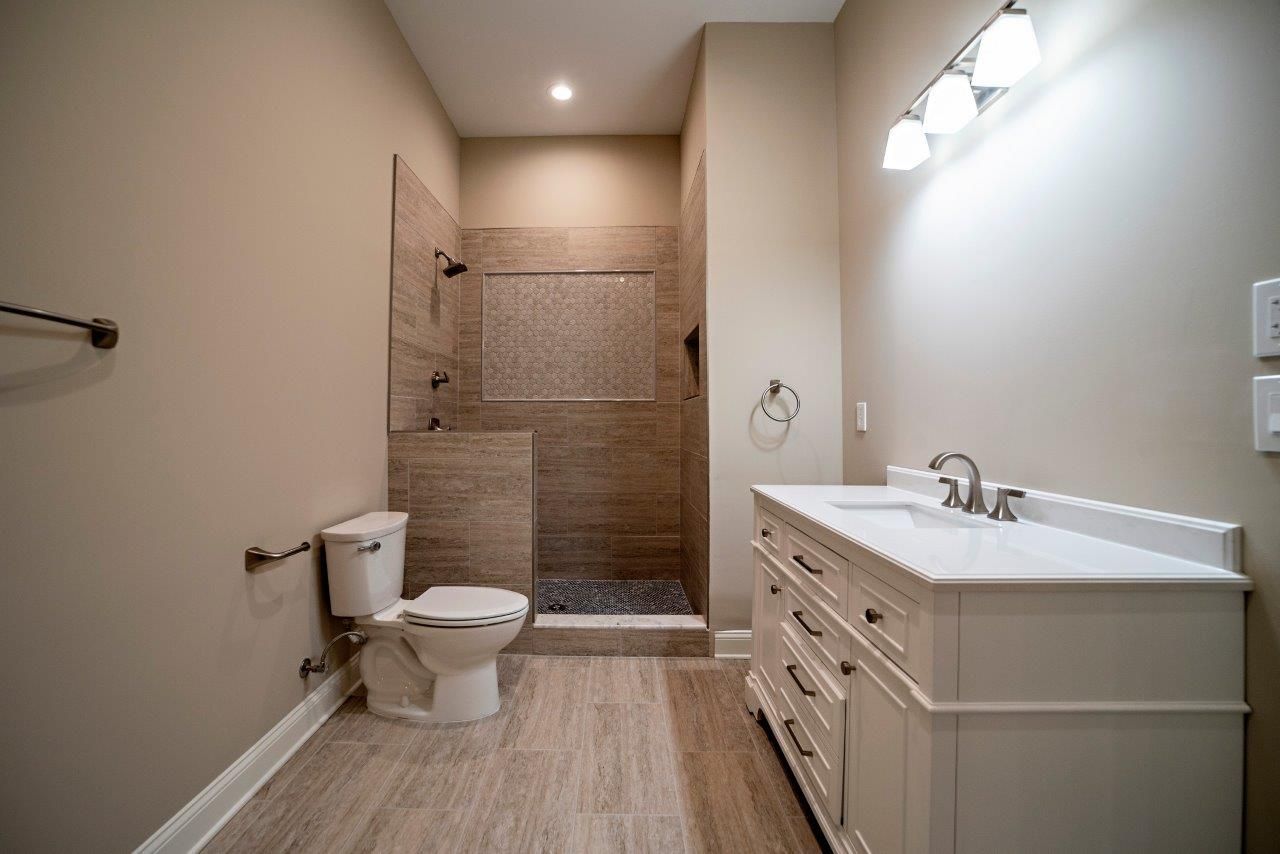 Bathroom with tan walls, shower, white vanity, toilet, and light fixture.