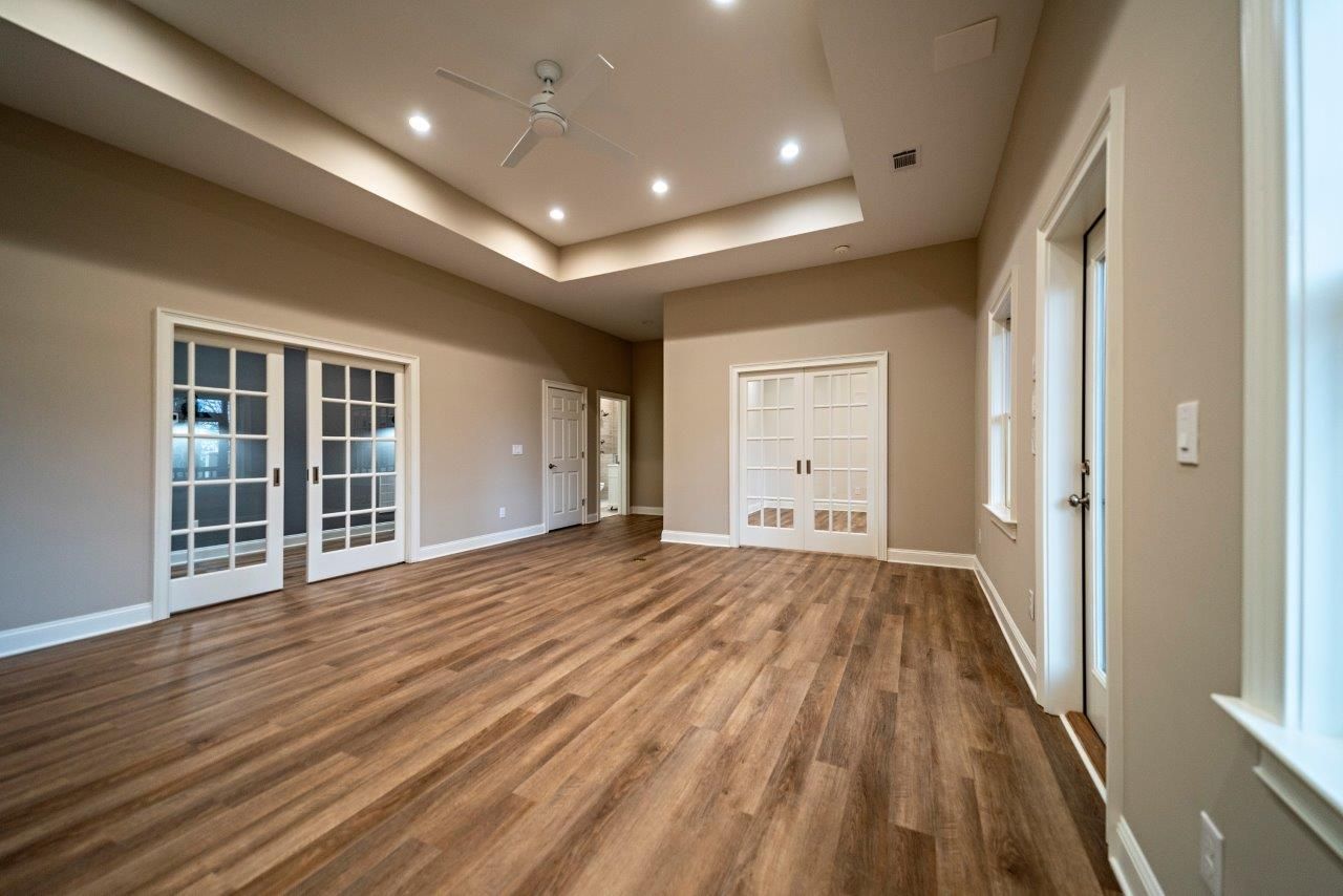 Empty room with hardwood floors, beige walls, and white doors and trim.