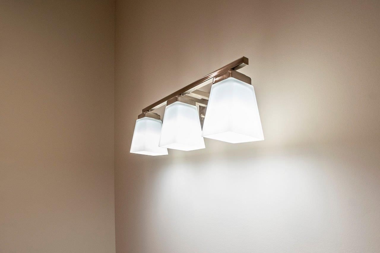 Three-light fixture with white shades on a light-colored wall.