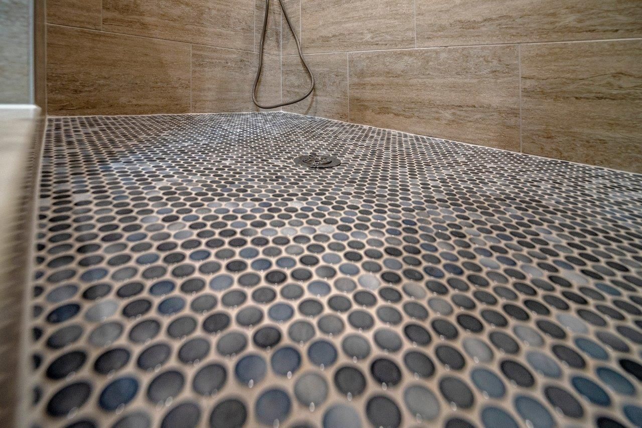 Shower floor with small, dark gray stone tiles. Tan stone tile walls.