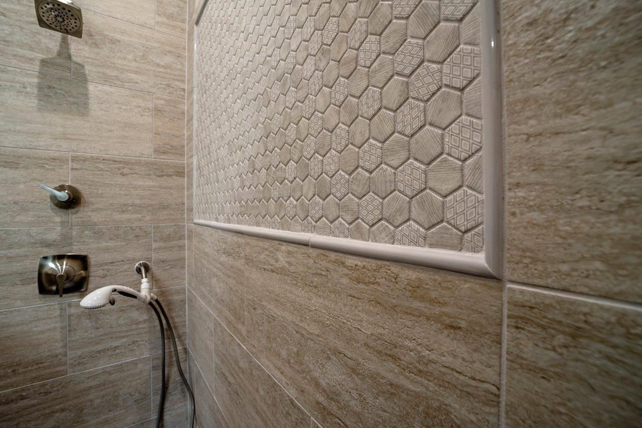 Shower interior with tan stone-like tiles and honeycomb tile accent framed with a thin white border.