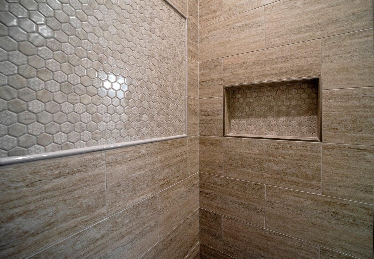 Shower interior with tan tiles and honeycomb tile accent, built-in shelf.