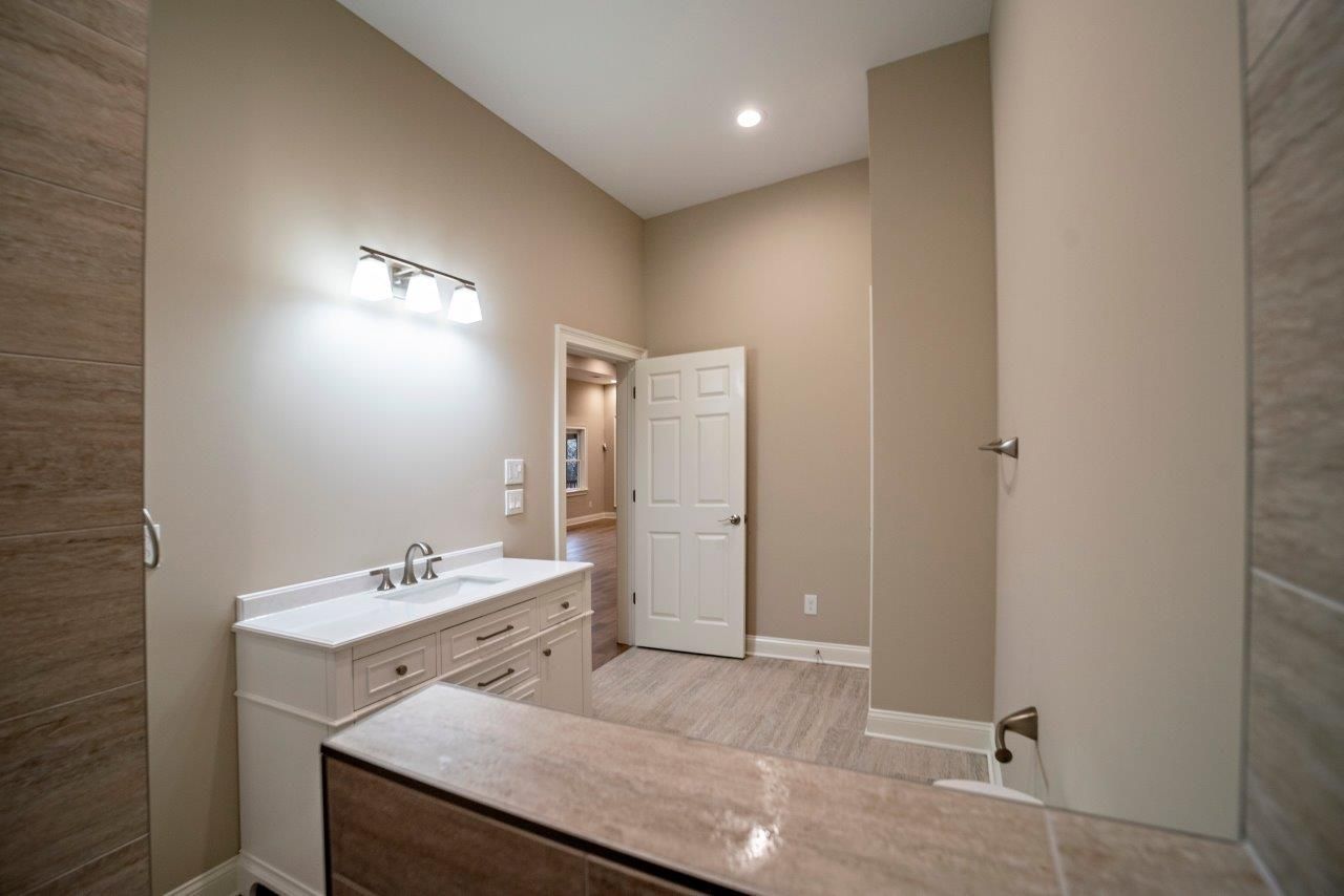 Bathroom with beige walls, white vanity, and light-colored tile. A door leads to another room.