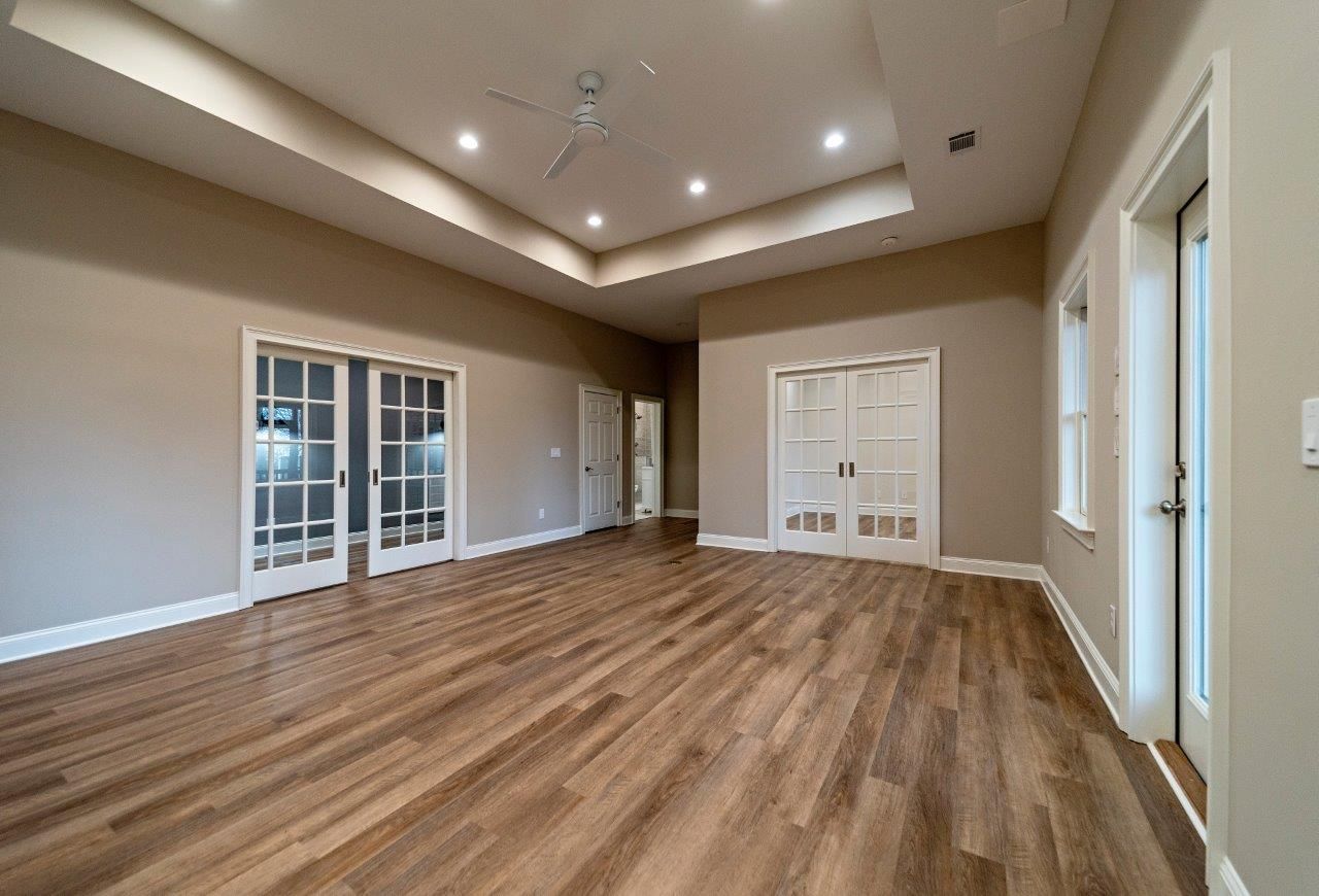 Empty room with wooden floors, French doors, and a recessed ceiling.