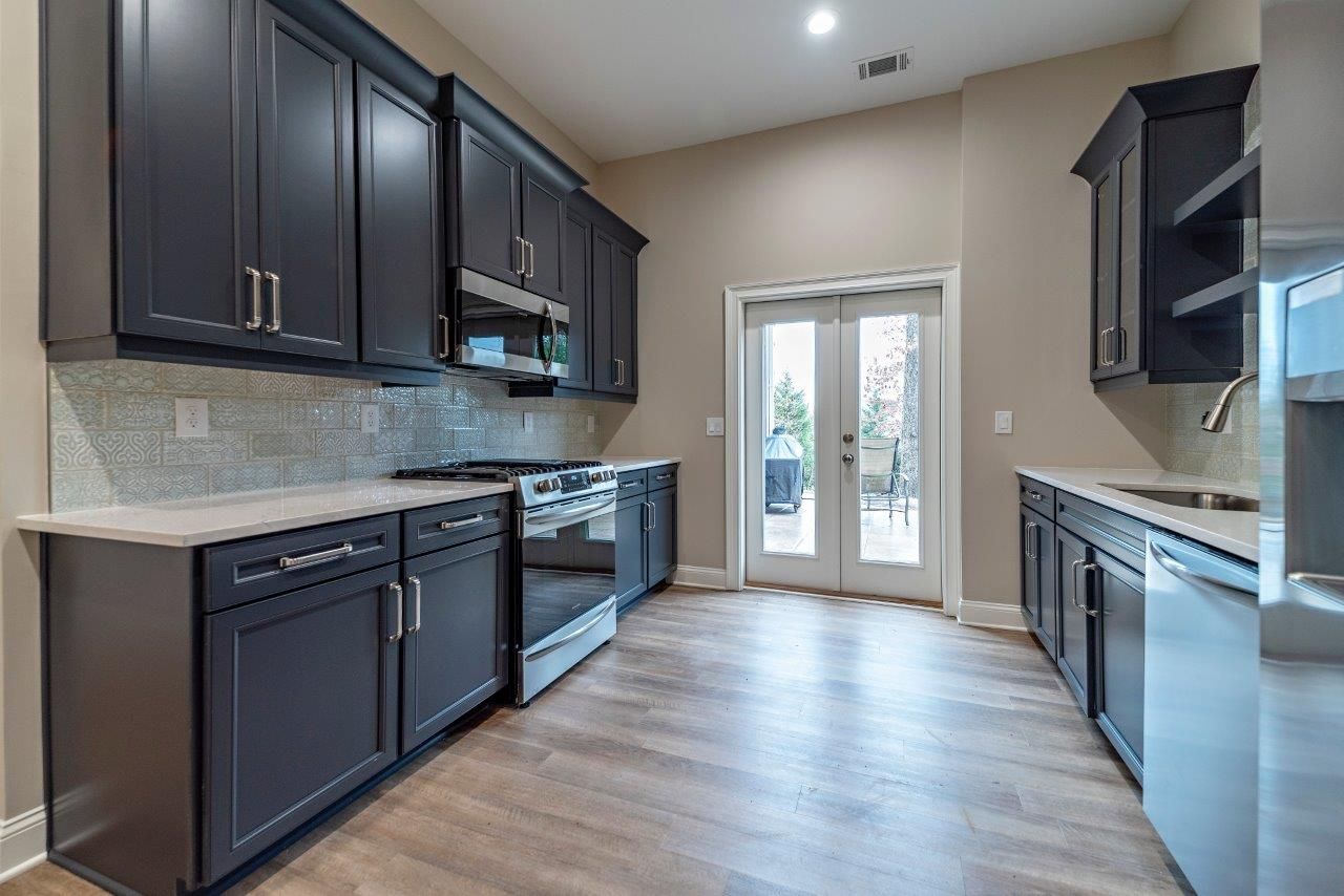Modern kitchen with dark blue cabinets, stainless steel appliances, and wood-look flooring.