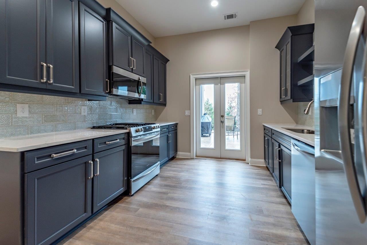 Dark gray kitchen cabinets with stainless steel appliances and light wood flooring.