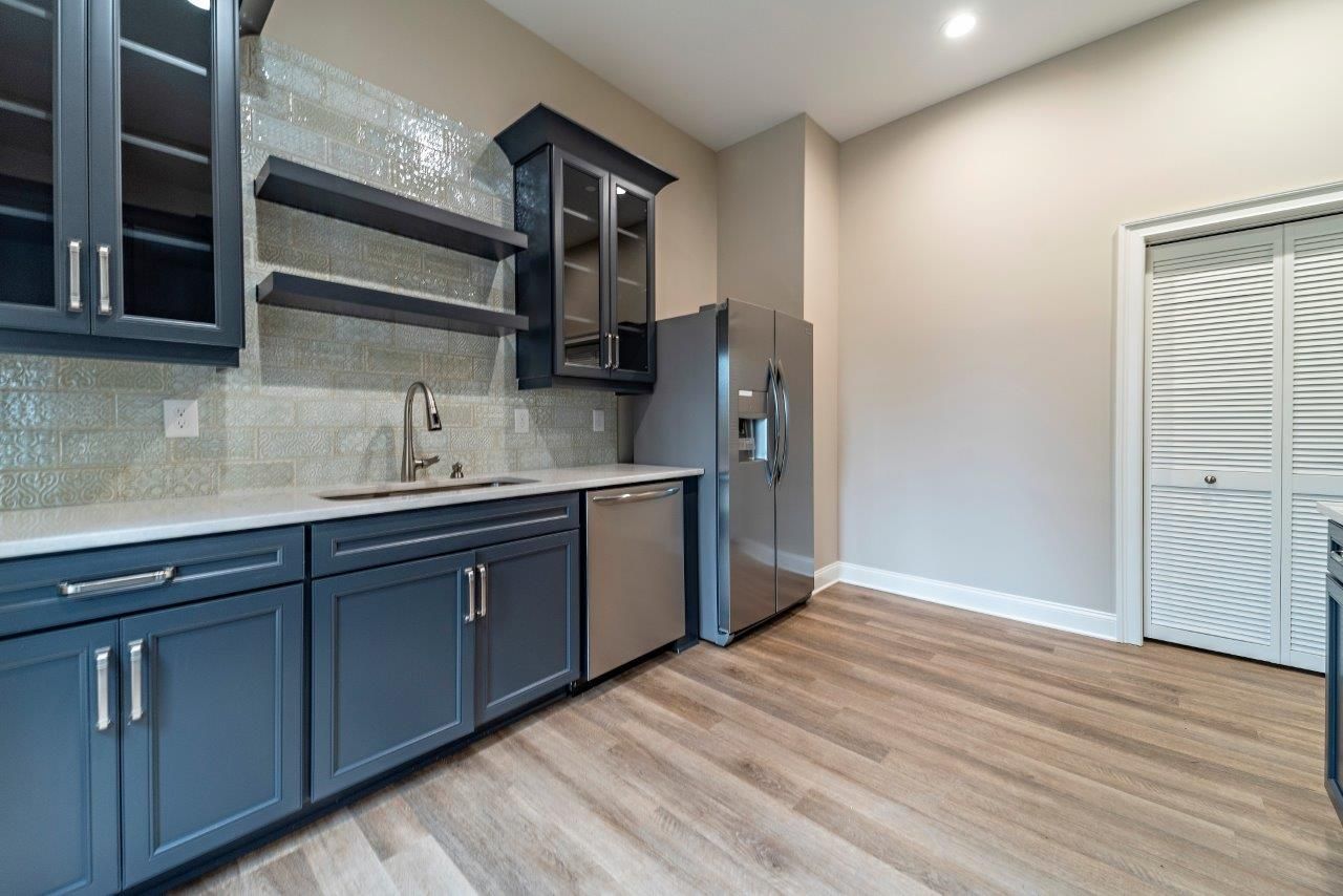 Modern kitchen with blue cabinets, stainless steel appliances, and wooden floor.