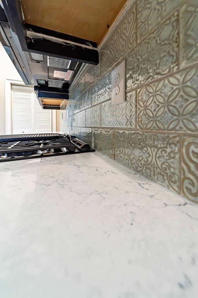Kitchen with patterned backsplash, white countertops, and range hood.
