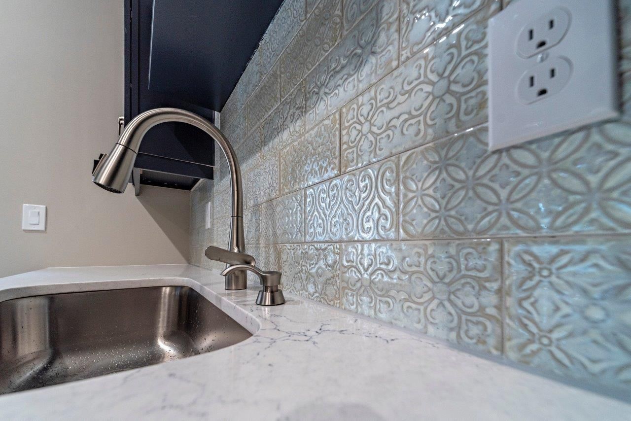 Stainless steel kitchen sink and faucet with patterned blue tile backsplash.