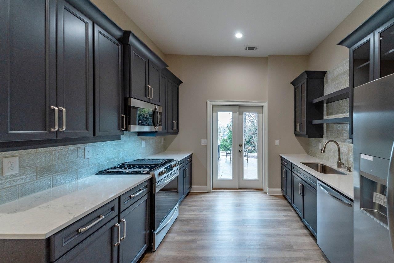 Modern kitchen with dark gray cabinets, white countertops, stainless steel appliances, and a glass door.