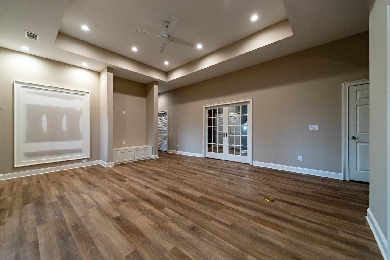 Empty room with wood floors, tan walls, and recessed lighting. Features include a ceiling fan and glass doors.