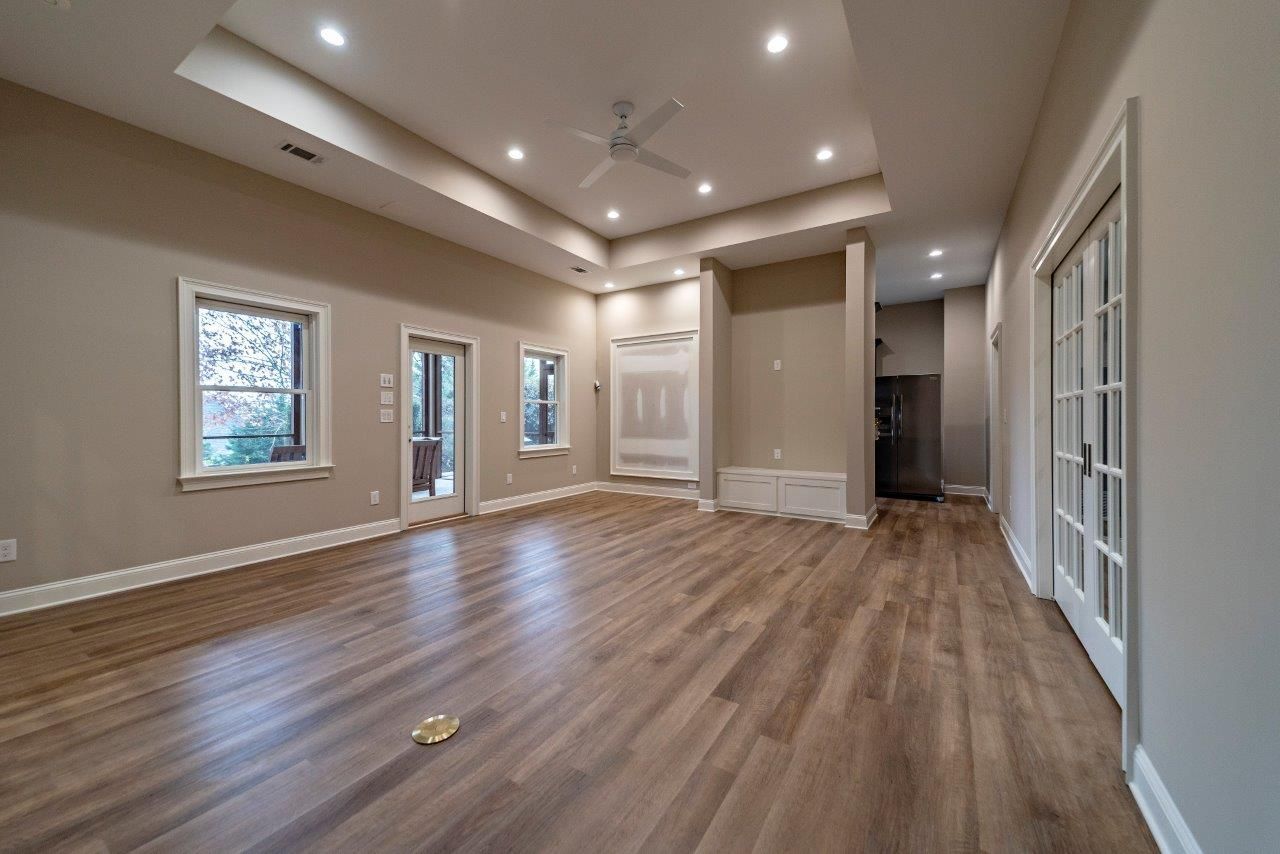 Empty room with wood floors, beige walls, recessed lighting, and a doorway.