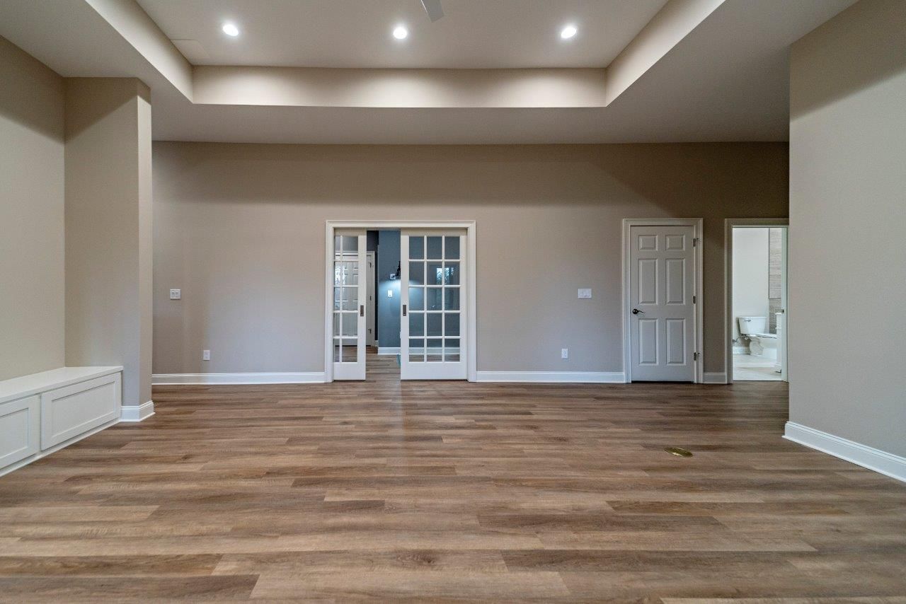 Empty room with wood floors, neutral walls, French doors, and recessed lighting.