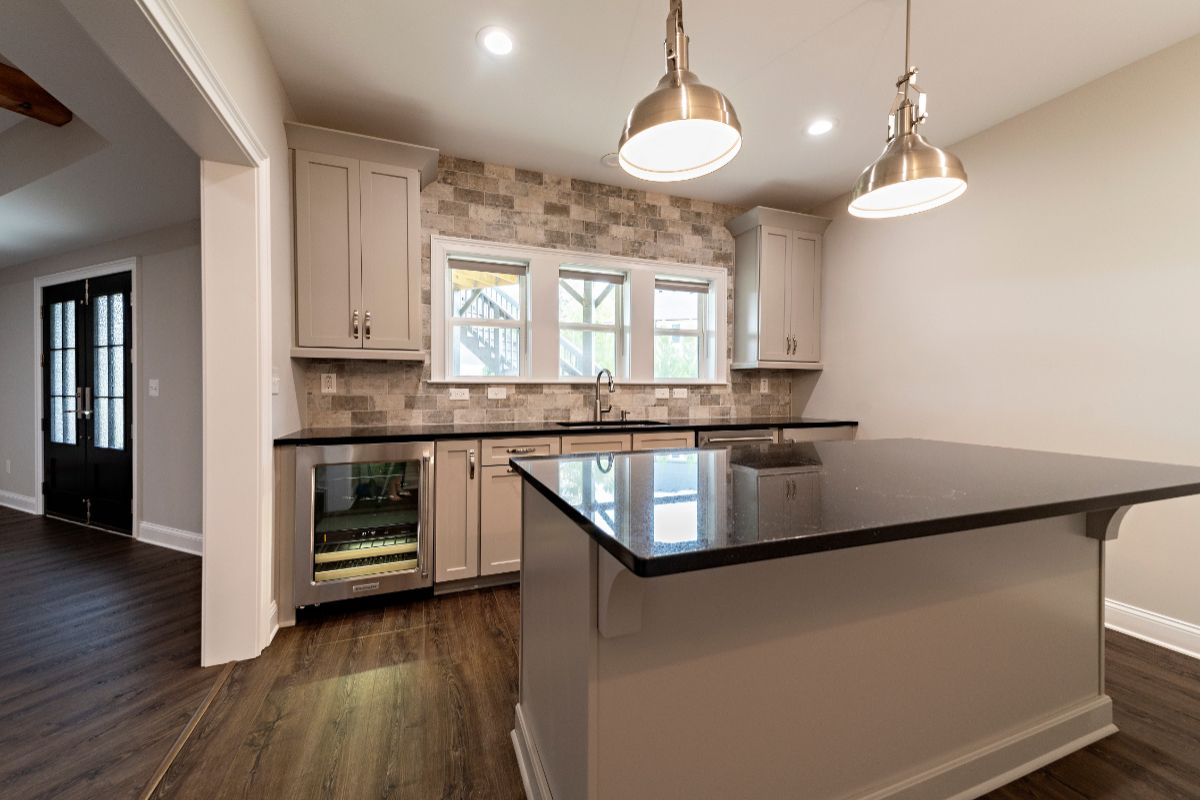Modern kitchen with light gray cabinets, black countertops, and island; stainless steel pendant lights.