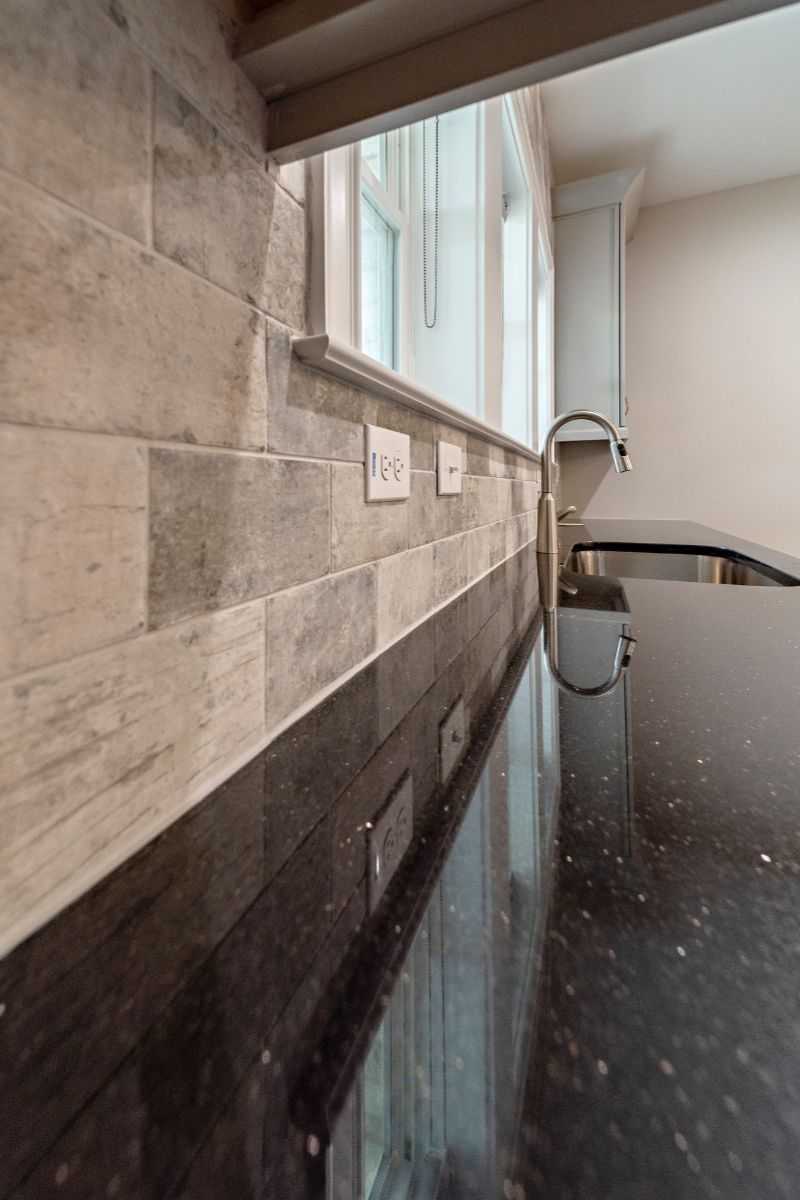 Black speckled countertop with gray and white tiled backsplash. Kitchen setting.