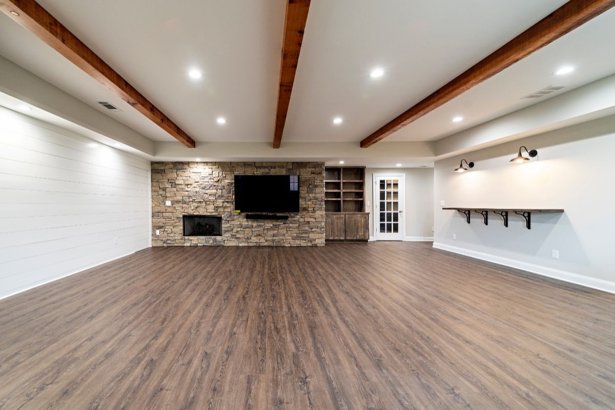 Spacious living area with wood-look flooring, stone fireplace, built-in shelving, and exposed ceiling beams.