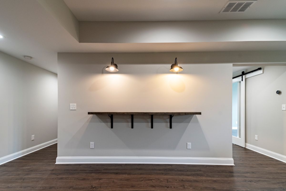 A wall with a dark wooden shelf and two lights, dark floors, and white walls.