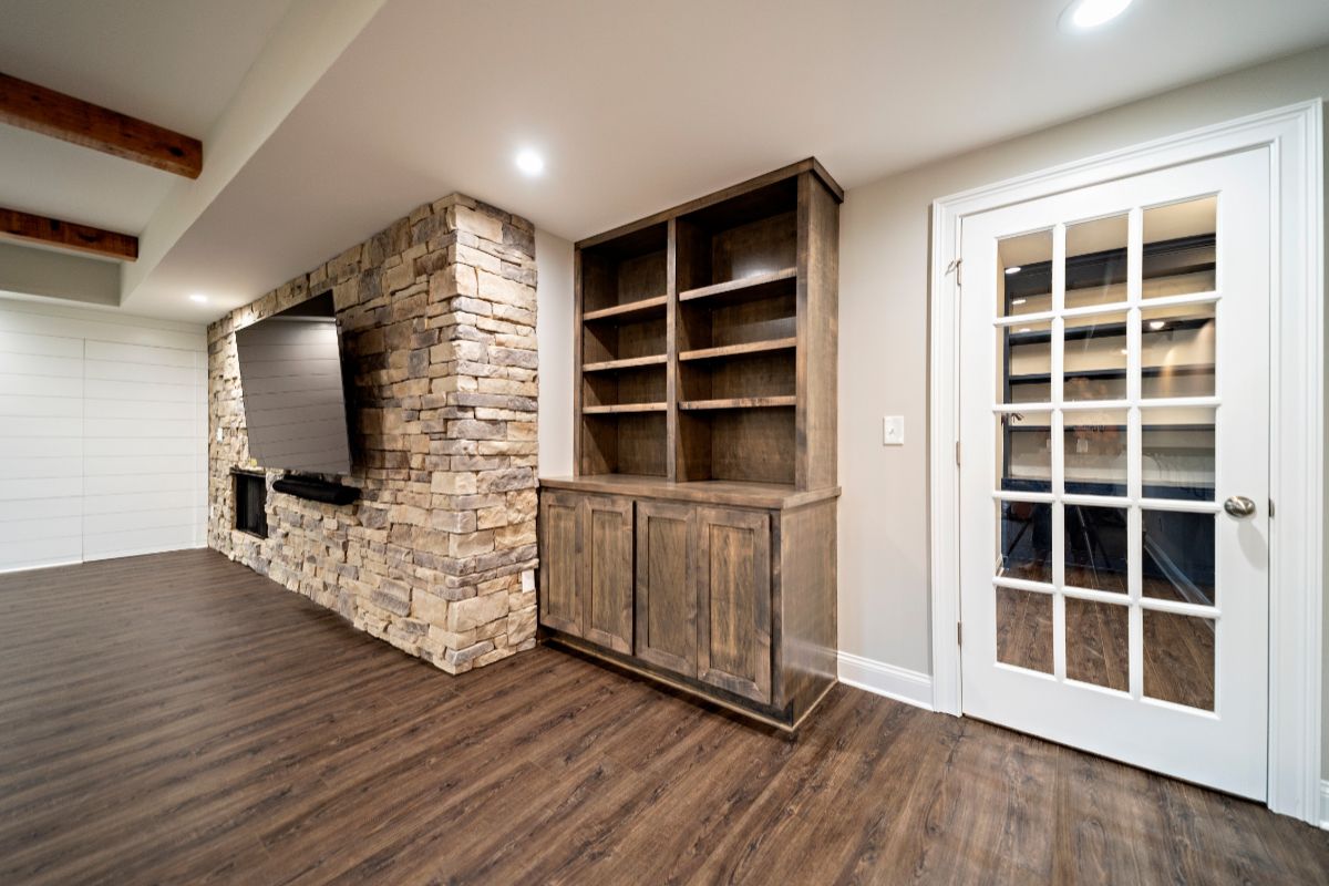 Basement entertainment room with a stone accent wall, built-in shelving, dark wood floor, and glass-paned door.