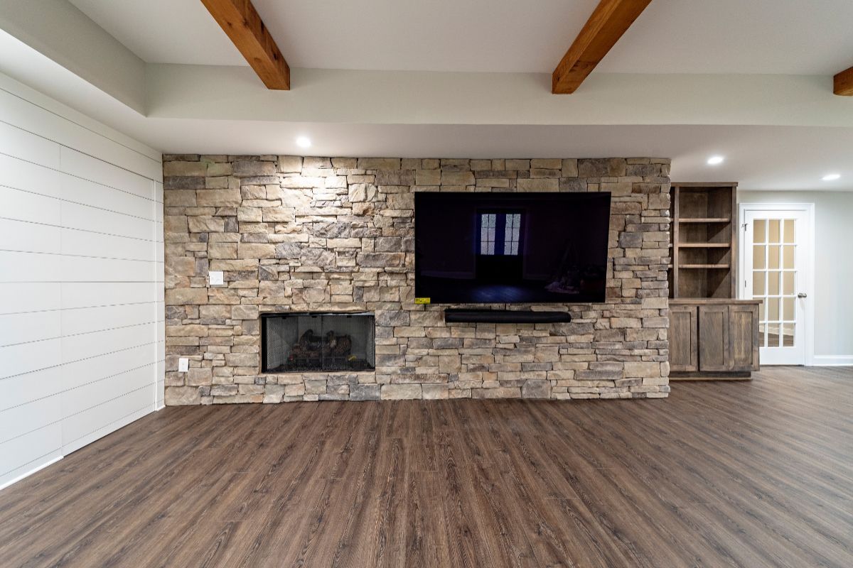 Living room with stone accent wall, fireplace, TV, wood beams, and built-in shelving.