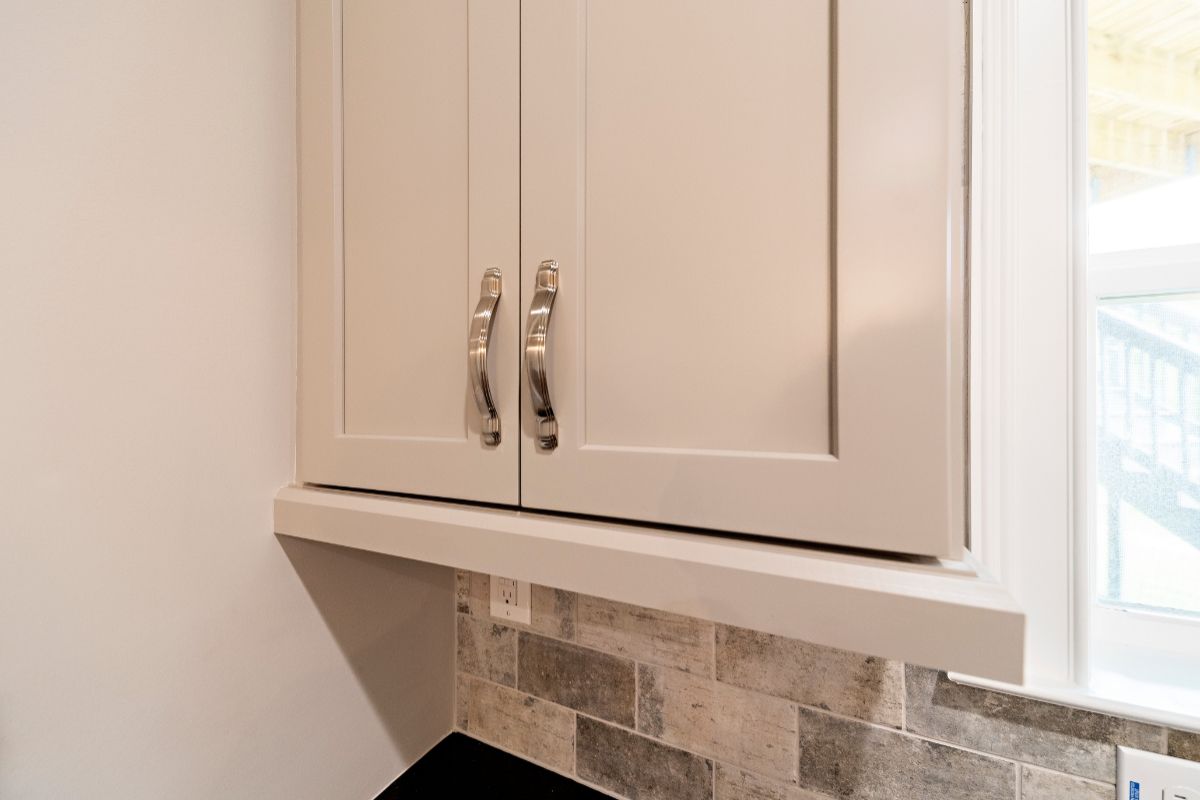 Gray kitchen cabinets with silver handles above a tiled backsplash and windowsill.