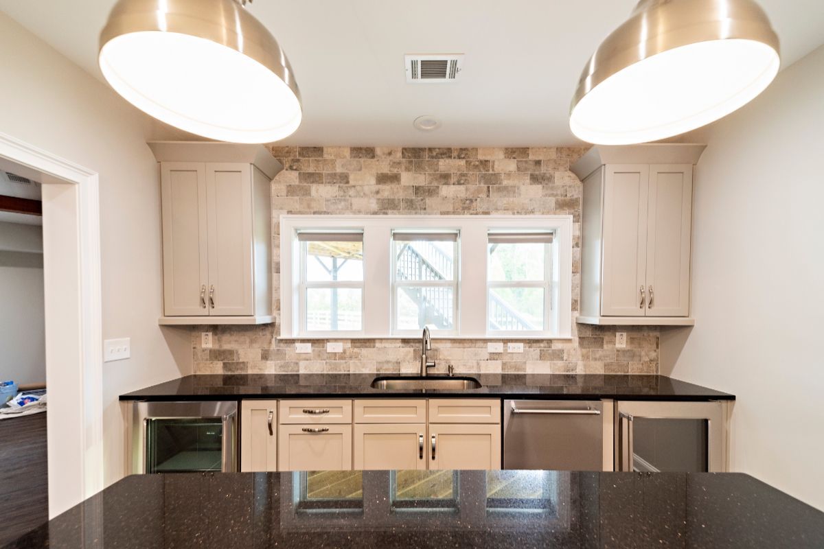 Kitchen area with cabinets, granite countertop, three windows, and two hanging lights.