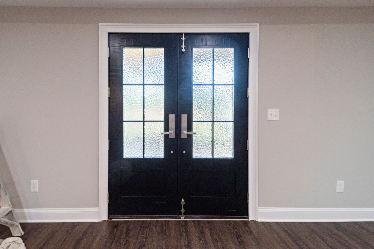 Double black doors with glass panels and silver handles set in a white-framed doorway, with light gray walls