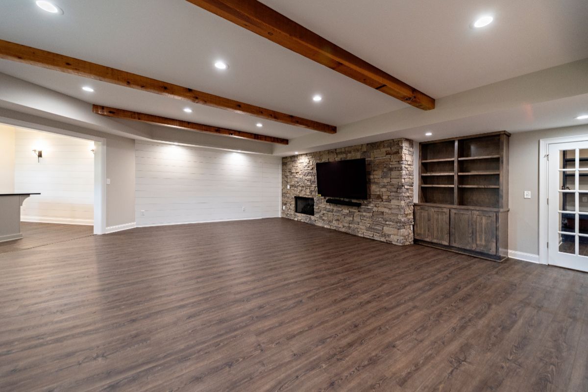 Spacious, finished basement with wood floors, stone fireplace, built-in shelving, and exposed wood beams.