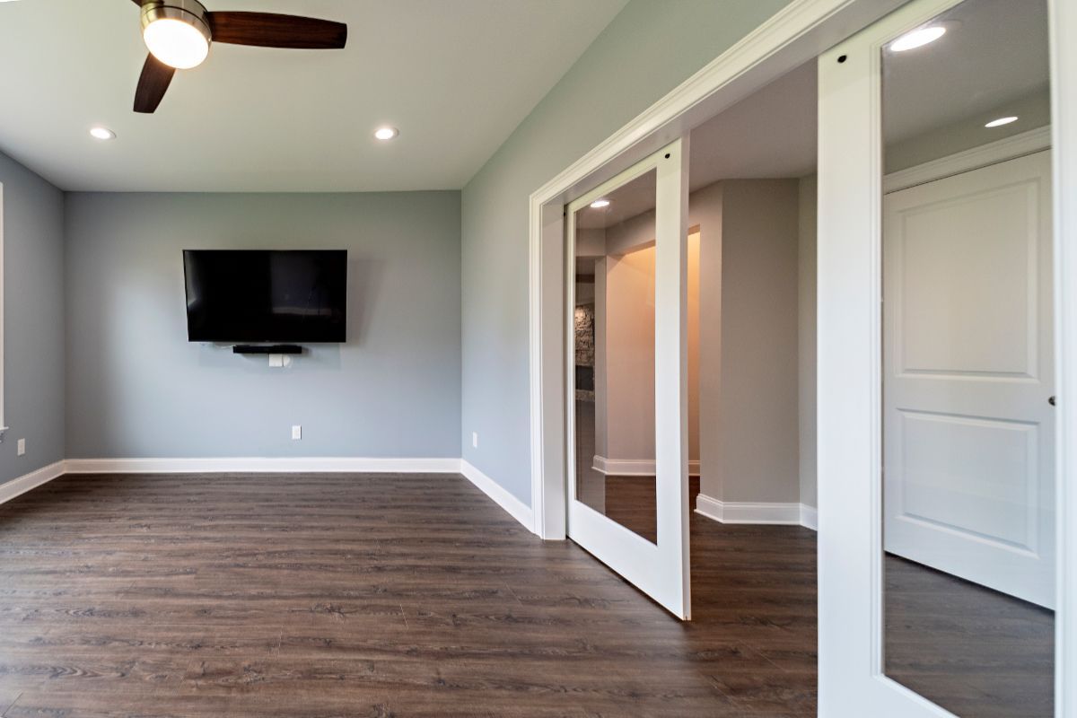 Empty room with gray walls, dark wood floor, and white sliding doors. TV mounted on the wall.