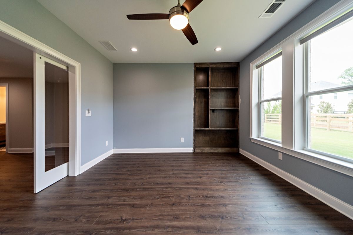 Empty room with dark wood floor, built-in shelving, blue-gray walls, and large windows.