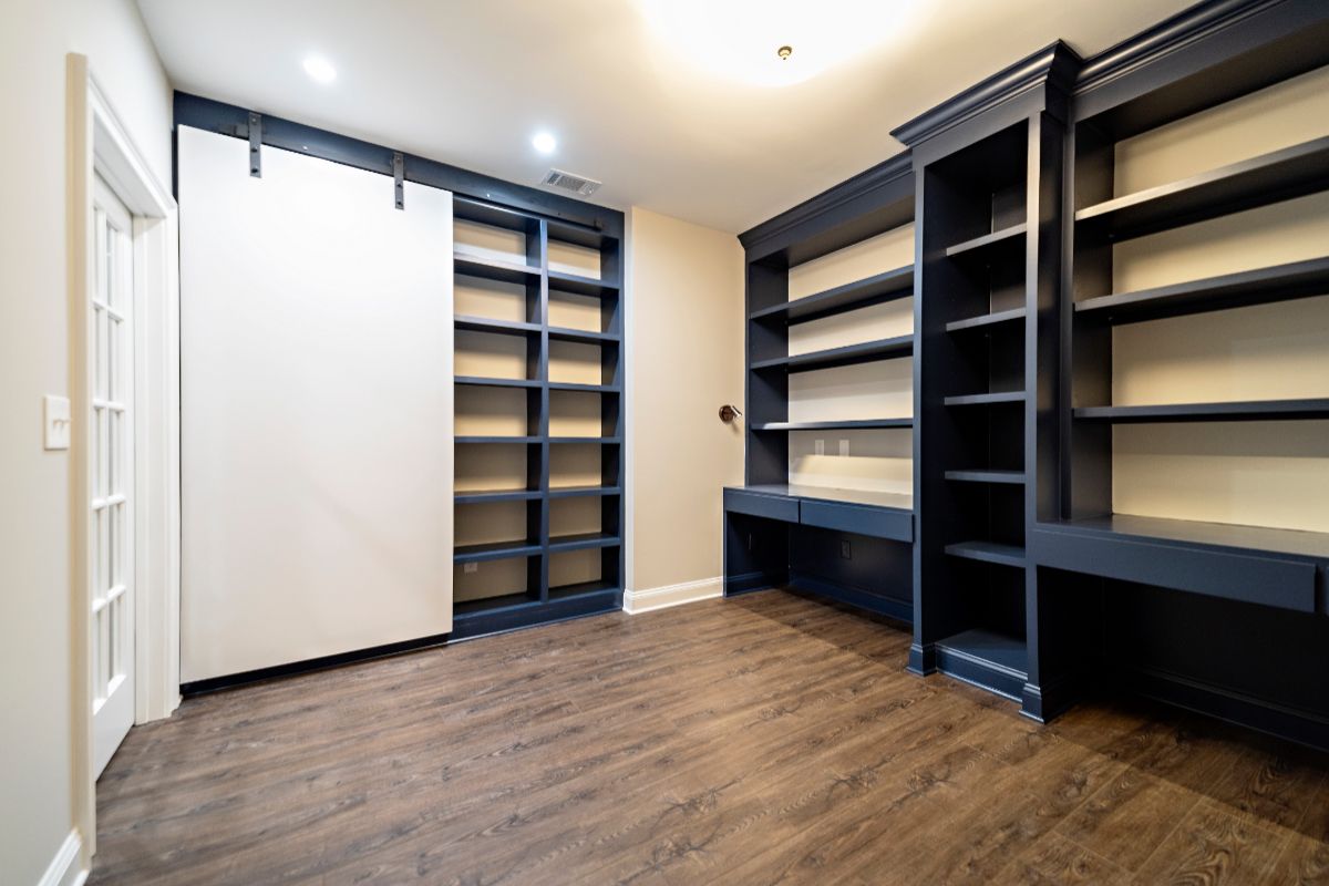 Office with built-in dark blue bookshelves and desks. A white sliding door covers more shelves. Wood-look flooring.