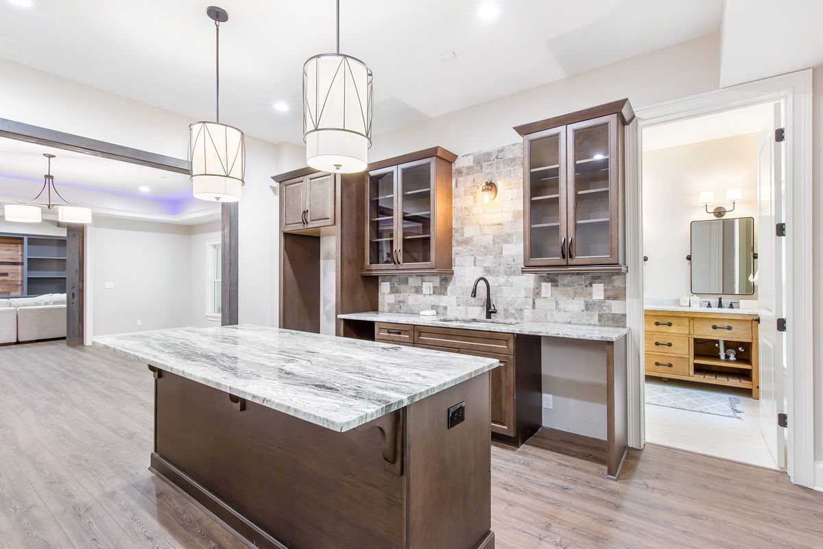 Modern kitchen with island, wooden cabinets, and white countertop, connected to bathroom with wood vanity.