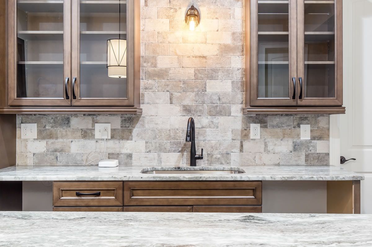 Kitchen with wooden cabinets, stone backsplash, sink, and pendant lighting.
