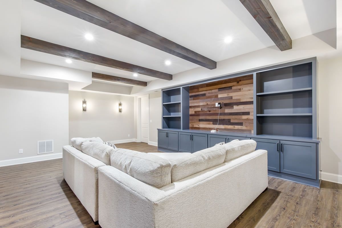 Modern living room with a gray sectional, built-in shelves, and wood ceiling beams.