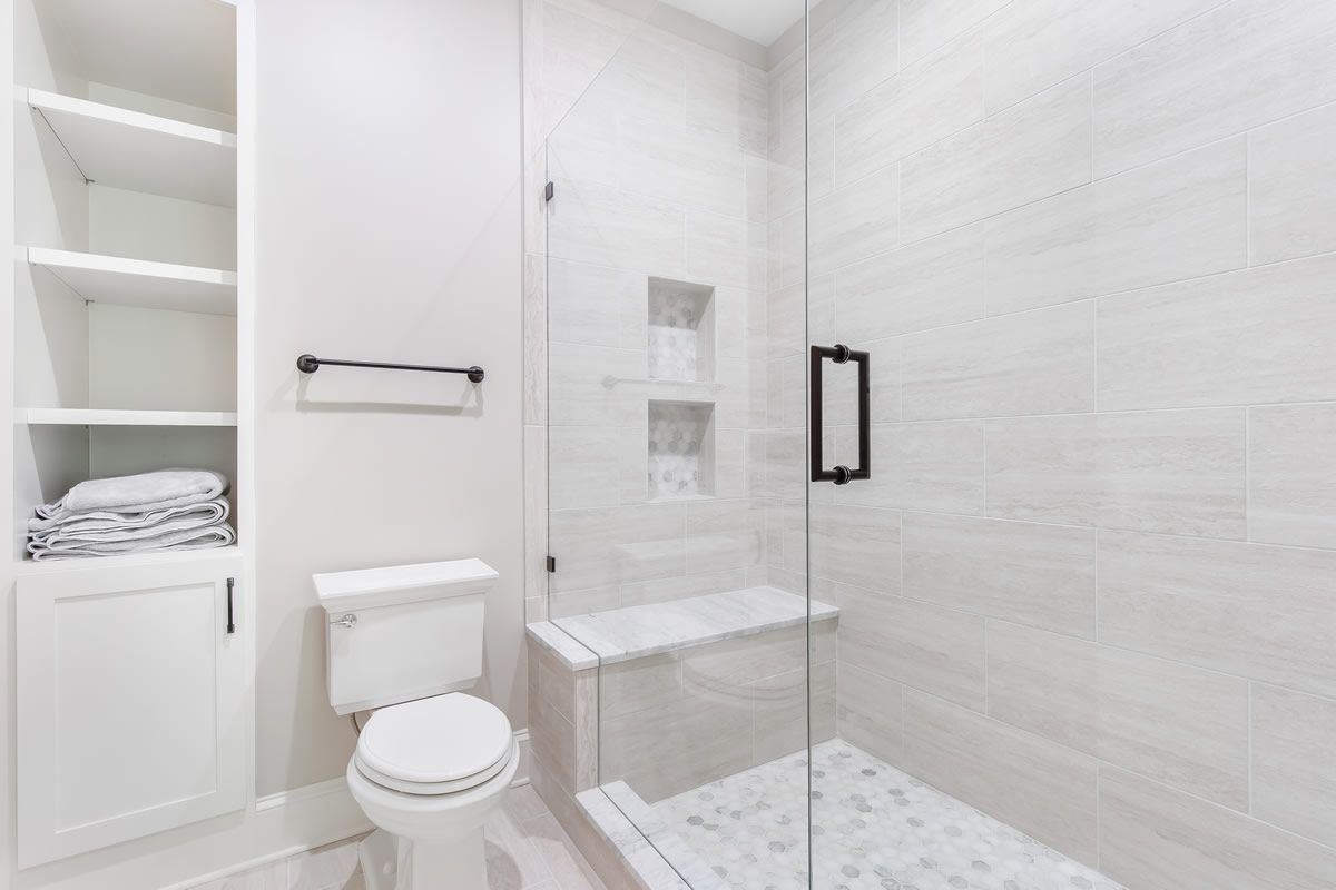 White bathroom with shower, toilet, and built-in shelving.