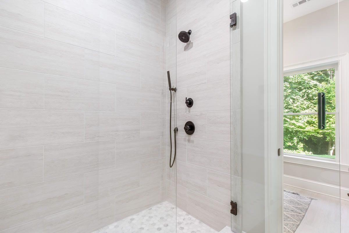 White tile shower with glass door and black fixtures.