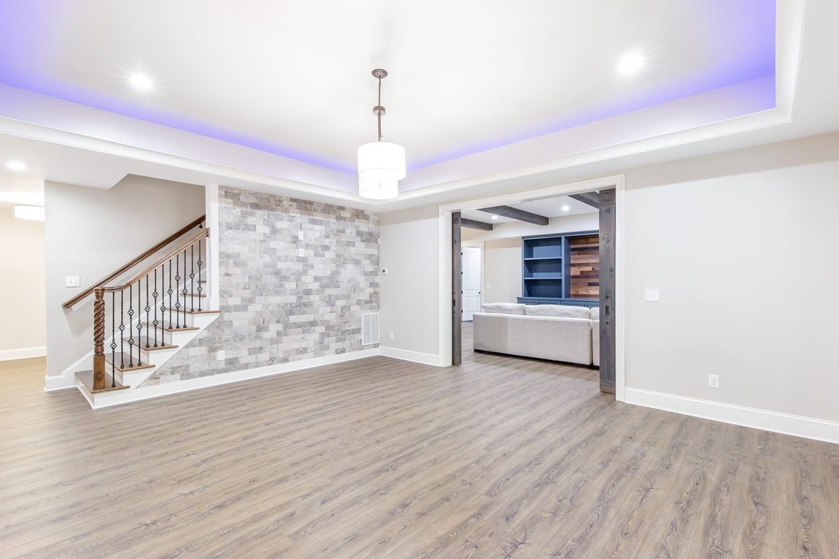 Empty finished basement with gray stone accent wall, stairs, and built-in shelving.