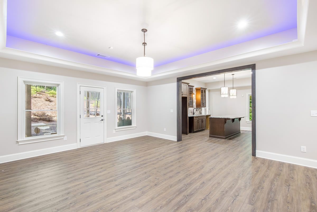 Empty room with wooden floors, white walls, and a view into a kitchen.